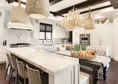 A white kitchen with marble counter tops and a chandelier.