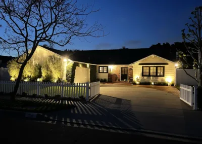 A home is lit up at night with a white picket fence.