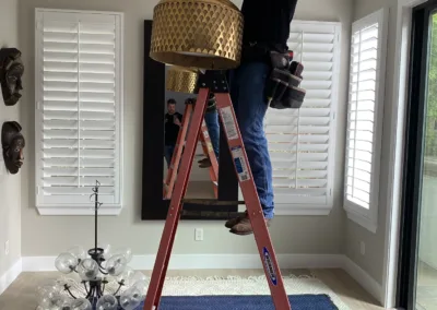 A man working on a ladder in a living room.